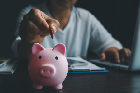 Business asian woman hand put coins in piggy bank on wood table background, saving money wealth and financial concept, finance, investment, Financial planning.Financial planning deposit for retirementの写真素材