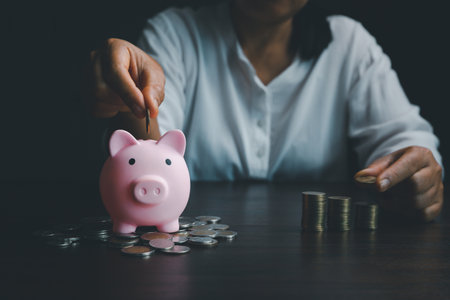 Business asian woman hand put coins in piggy bank on wood table background, saving money wealth and financial concept, finance, investment, Financial planning.Financial planning deposit for retirementの写真素材