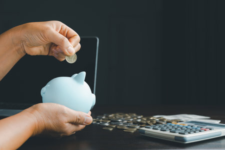 Business asian woman hand put coins in piggy bank on wood table background, saving money wealth and financial concept, finance, investment, Financial planning.Financial planning deposit for retirementの写真素材