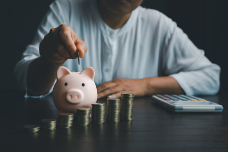 Business asian woman hand put coins in piggy bank on wood table background, saving money wealth and financial concept, finance, investment, Financial planning.Financial planning deposit for retirementの写真素材