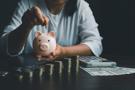 Business asian woman hand put coins in piggy bank on wood table background, saving money wealth and financial concept, finance, investment, Financial planning.Financial planning deposit for retirementの写真素材