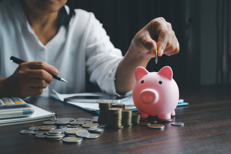 Business asian woman hand put coins in piggy bank on wood table background, saving money wealth and financial concept, finance, investment, Financial planning.Financial planning deposit for retirementの写真素材