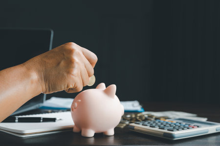 Business asian woman hand put coins in piggy bank on wood table background, saving money wealth and financial concept, finance, investment, Financial planning.Financial planning deposit for retirementの写真素材