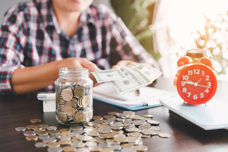 Coins in glass jar with business woman hand calculating expenses, saving money wealth and financial...