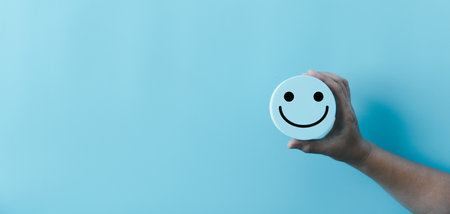 Woman hand holding happy face smile face icon on round blue object. Customer experience and service with satisfaction concept. positive thinking, mental health assessment, world mental health day.の写真素材