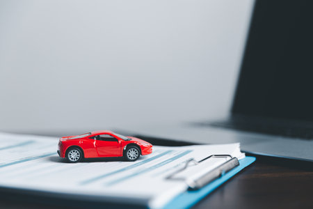 Business woman's hand protecting red toy car on desk. Planning to manage transportation finance costs. Concept of car insurance business, saving buy - sale with tax and loan for new car.の写真素材
