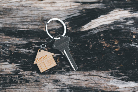 House key on a house shaped keychain resting on wooden floorboards concept for real estate renting property. House model and key in house door. Real estate agent offer house, property insurance.の写真素材