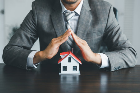 Property insurance and security concept. Protecting gesture of man and symbol of house. Estate agent giving house keys to woman and asked customer to sign the documents to make the contract legally.の写真素材