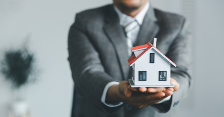 Property insurance and security concept. Protecting gesture of man and symbol of house. Estate agent giving house keys to woman and asked customer to sign the documents to make the contract legally.の写真素材