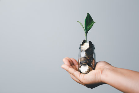 The green plant grow on coin stack is a business growth concept. The hand that is holding coin tree...