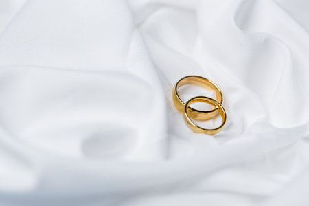 Golden wedding rings for engagement. Marriage golden rings with white, pink ribbons background....