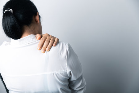 A business office worker is an asian woman is sitting in front of the laptop computer. A businesswoman stressing her body part fingers, hands arm. A femaleOffice manager is exhausted at her workplace.の写真素材