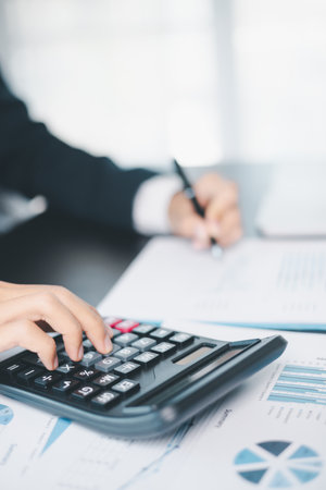 Business professional working with financial documents and calculator, analyzing financial data and...