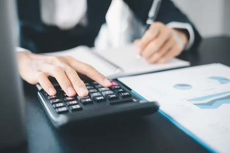 Business professional using calculator while analyzing financial reports and graphs for investment planning and financial management.の写真素材