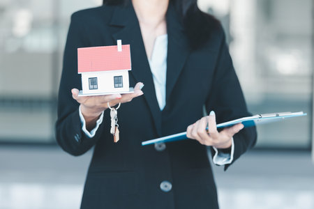 Woman hand hold key buy home model business concept involves sell financial management investment bank loan ownership income economy finance investments purchasing apartment blur background estateの写真素材