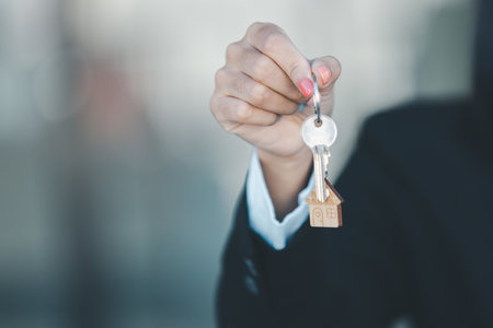 Woman hand hold key buy home model business concept involves sell financial management investment bank loan ownership income economy finance investments purchasing apartment blur background estateの写真素材