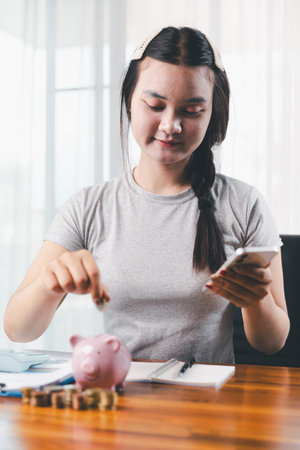 Businesswoman saving money with piggy bank and coins on desk, financial planning and investment concept. Young Asian woman making stack of coin. invest save finance, saving money, investmentの写真素材