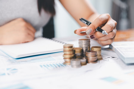 Young Asian woman making stack of coins. Invest, save finance concept, saving money, investment. Dollar bills on table with pile of coins and banks calculator, money to save and invest to make income.の写真素材