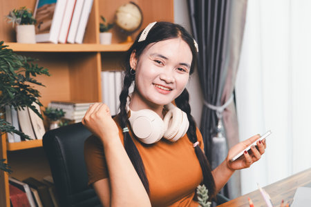 Asian girl doing homework and studying at home. woman using laptop at desk write notes watching webinar, study online, look at learn web class or having virtual call meeting remote working from home.の写真素材
