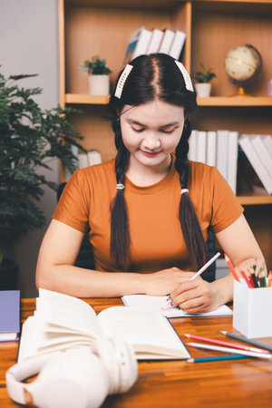 Asian girl doing homework and studying at home. woman using laptop at desk write notes watching webinar, study online, look at learn web class or having virtual call meeting remote working from home.の写真素材
