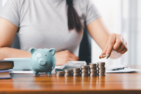 Businesswoman saving money with piggy bank and coins on desk, financial planning and investment concept. Young Asian woman making stack of coin. invest save finance, saving money, investmentの写真素材