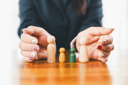 Hands protecting family wooden model for insurance and assurance life concept. Businessman hand gesture protecting wooden domino falling to family dolls for insurance and assurance.の写真素材