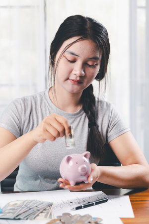 Businesswoman saving money with piggy bank and coins on desk, financial planning and investment concept. Young Asian woman making stack of coin. invest save finance, saving money, investmentの写真素材