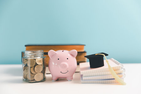 Concept of saving money for education, student loan, scholarship in future. Piggy bank with graduation hat, stack of coins. Earth globe with graduation hat, on table. Tuition feesの写真素材