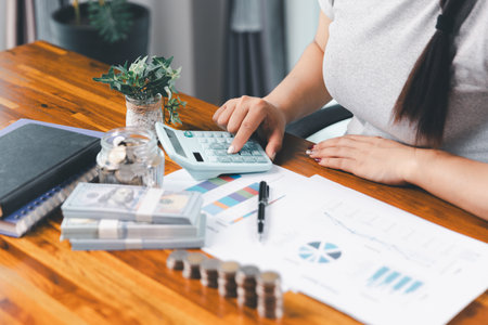 Young Asian woman making stack of coin. invest save finance concept, saving money, investment. dollar bills on table with pile of coins and banks calculator, money to save and invest to make income.の写真素材
