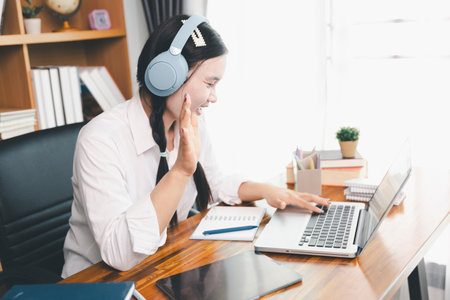 Asian girl student wear headphones learning online watching webinar class looking at laptop computer elearning remote lesson making notes or video calling virtual conference meeting teacher at home.の写真素材