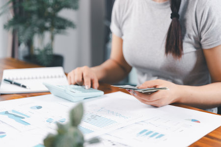 Young Asian woman making stack of coin. invest save finance concept, saving money, investment. dollar bills on table with pile of coins and banks calculator, money to save and invest to make income.の写真素材