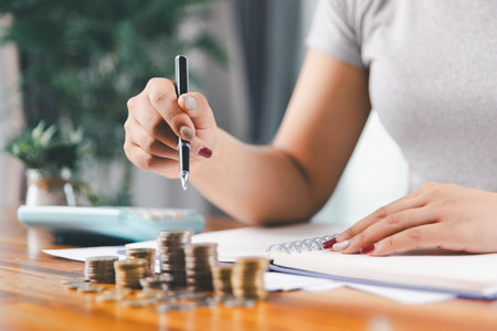 Young Asian woman making stack of coin. invest save finance concept, saving money, investment. dollar bills on table with pile of coins and banks calculator, money to save and invest to make income.の写真素材