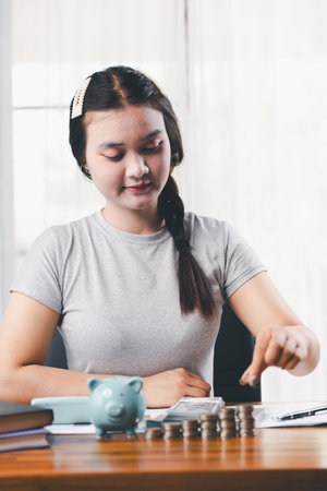 Businesswoman saving money with piggy bank and coins on desk, financial planning and investment concept. Young Asian woman making stack of coin. invest save finance, saving money, investmentの写真素材