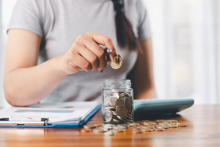 Businesswoman saving money with piggy bank and coins on desk, financial planning and investment concept. Young Asian woman making stack of coin. invest save finance, saving money, investmentの写真素材