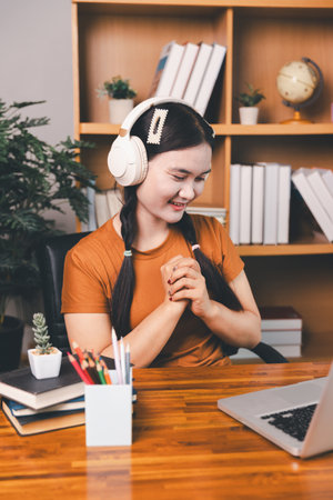 Asian girl doing homework and studying at home. woman using laptop at desk write notes watching webinar, study online, look at learn web class or having virtual call meeting remote working from home.の写真素材