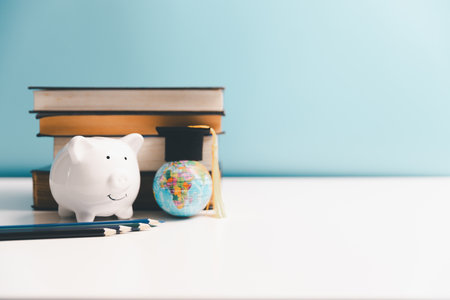 Concept of saving money for education, student loan, scholarship in future. Piggy bank with graduation hat, stack of coins. Earth globe with graduation hat, dollar banknotes on table.の写真素材