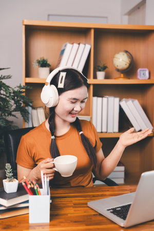 Asian girl doing homework and studying at home. woman using laptop at desk write notes watching webinar, study online, look at learn web class or having virtual call meeting remote working from home.の写真素材