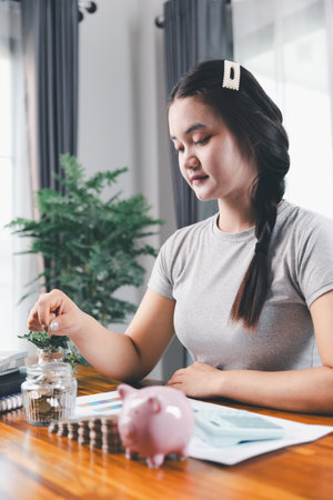 Businesswoman saving money with piggy bank and coins on desk, financial planning and investment concept. Young Asian woman making stack of coin. invest save finance, saving money, investmentの写真素材