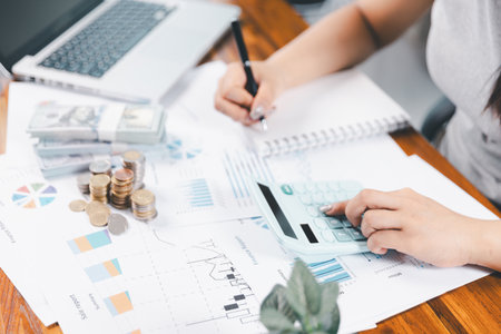 Young Asian woman making stack of coin. invest save finance concept, saving money, investment. dollar bills on table with pile of coins and banks calculator, money to save and invest to make income.の写真素材