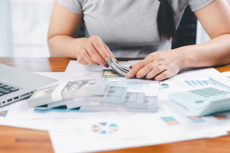 Young Asian woman making stack of coin. invest save finance concept, saving money, investment. dollar bills on table with pile of coins and banks calculator, money to save and invest to make income.の写真素材