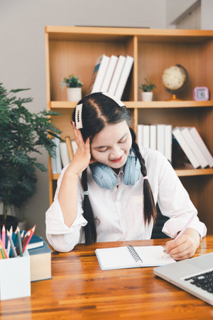 Asian girl student wear headphones learning online watching webinar class looking at laptop computer elearning remote lesson making notes or video calling virtual conference meeting teacher at home.の写真素材