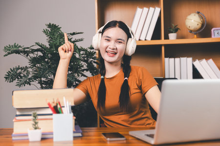 Asian girl doing homework and studying at home. woman using laptop at desk write notes watching...