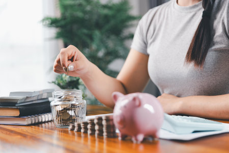 Businesswoman saving money with piggy bank and coins on desk, financial planning and investment concept. Young Asian woman making stack of coin. invest save finance, saving money, investmentの写真素材