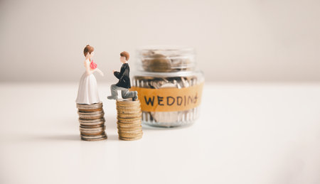 Save money for wedding and planning wedding concept. Sustainable financial goal for family life or married life. Miniature wedding on rows of rising coins, depicts savings or growth for new family.の写真素材