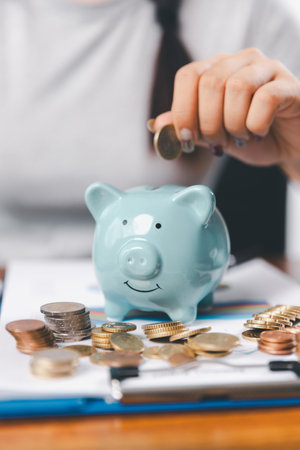 Businesswoman saving money with piggy bank and coins on desk, financial planning and investment concept. Young Asian woman making stack of coin. invest save finance, saving money, investmentの写真素材