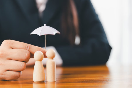 Hands protecting family wooden model for insurance and assurance life concept. Businessman hand gesture protecting wooden domino falling to family dolls for insurance and assurance.の写真素材