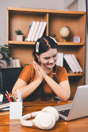 Asian girl doing homework and studying at home. woman using laptop at desk write notes watching webinar, study online, look at learn web class or having virtual call meeting remote working from home.の写真素材