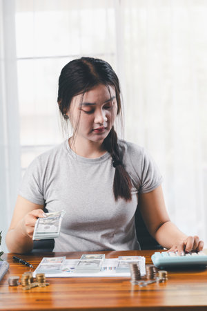 Young Asian woman making stack of coin. invest save finance concept, saving money, investment. dollar bills on table with pile of coins and banks calculator, money to save and invest to make income.の写真素材