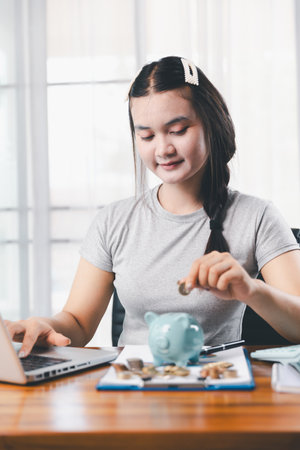 Businesswoman saving money with piggy bank and coins on desk, financial planning and investment concept. Young Asian woman making stack of coin. invest save finance, saving money, investmentの写真素材