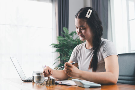 Businesswoman saving money with piggy bank and coins on desk, financial planning and investment concept. Young Asian woman making stack of coin. invest save finance, saving money, investmentの写真素材